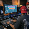 Person working in a music studio with audio equipment and a computer screen displaying music software wearing the producer drip not sorry dad hat